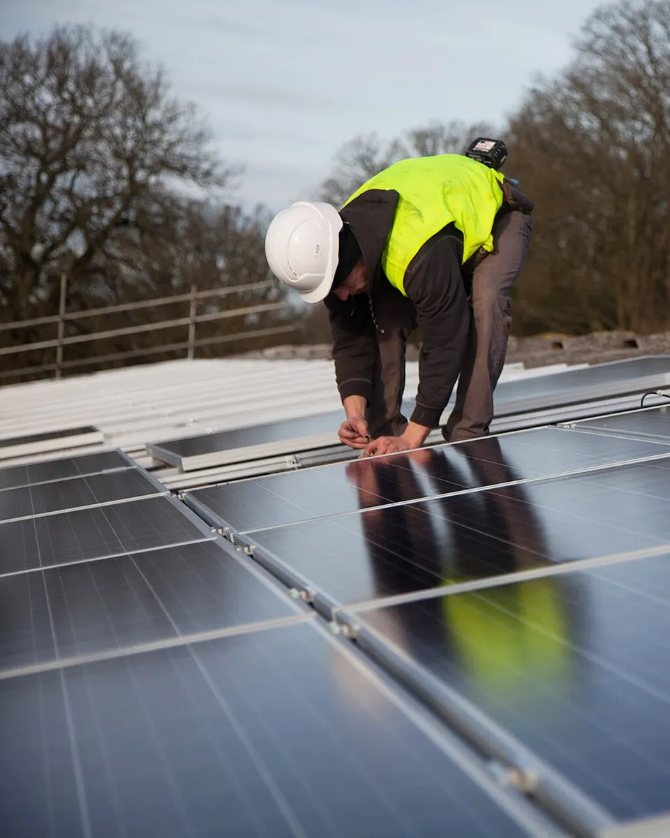 Monteur in Warnweste und Helm verschraubt Solarmodule auf einem Dach